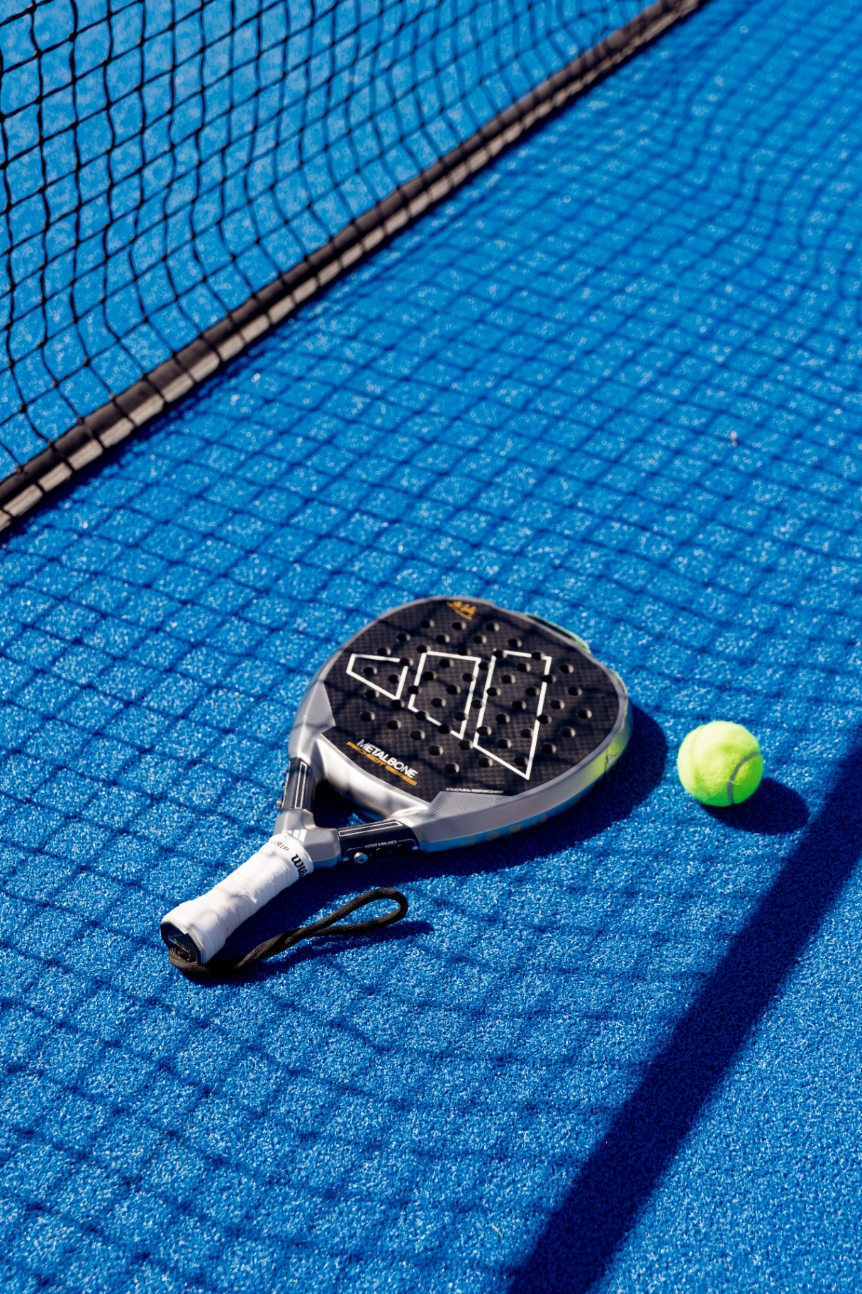 Overhead view of a padel racket and ball on a blue padel court beside the net