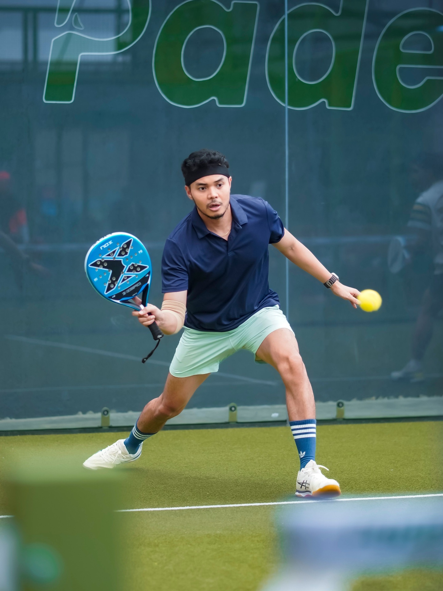 Padel player in mid-swing on an outdoor court returning a forehand